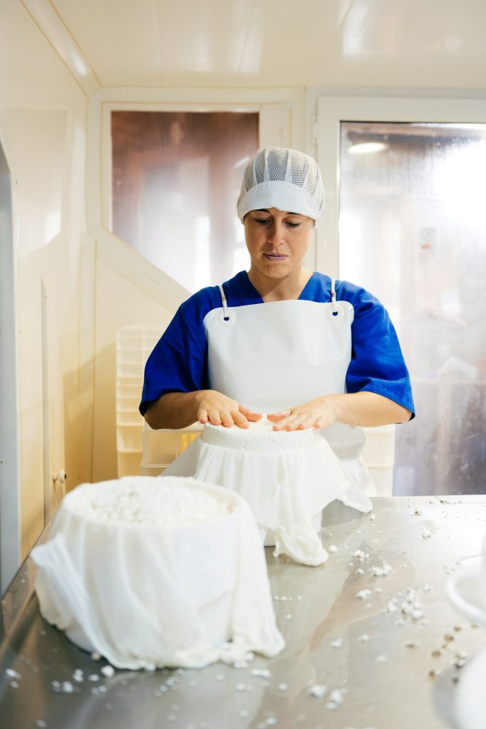 Female worker straining cottage cheese at factory